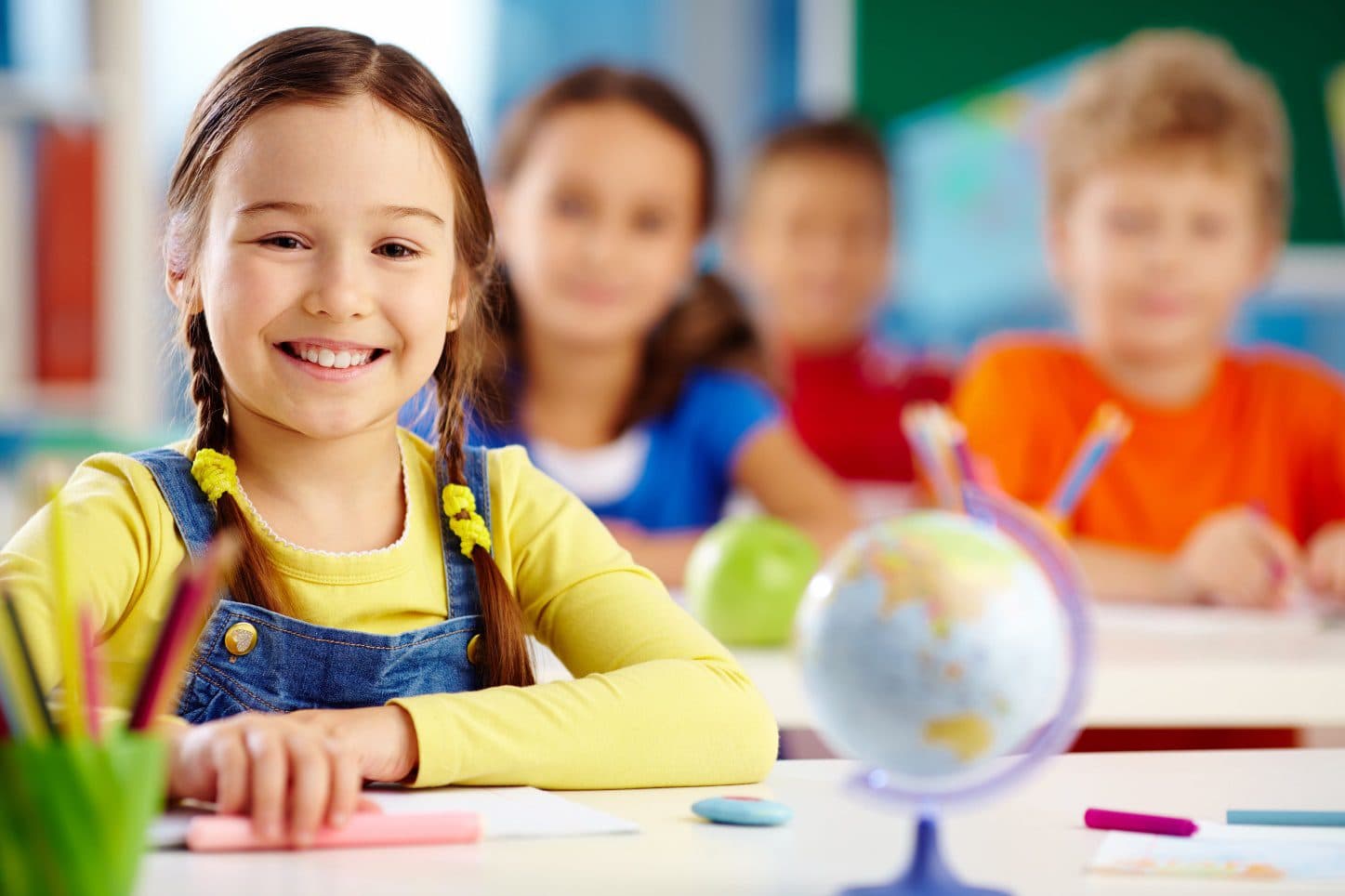 A smiling Pre-K student at her desk in a Kid's Country classroom